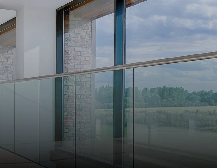 Modern glass balcony railing with stainless steel handrail beside large floor-to-ceiling windows.