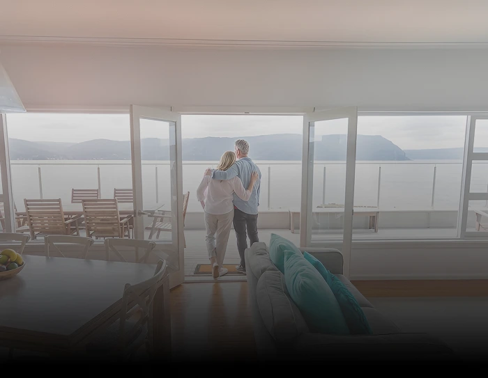 Bright modern living room with ocean-view balcony and couple standing near large glass doors.