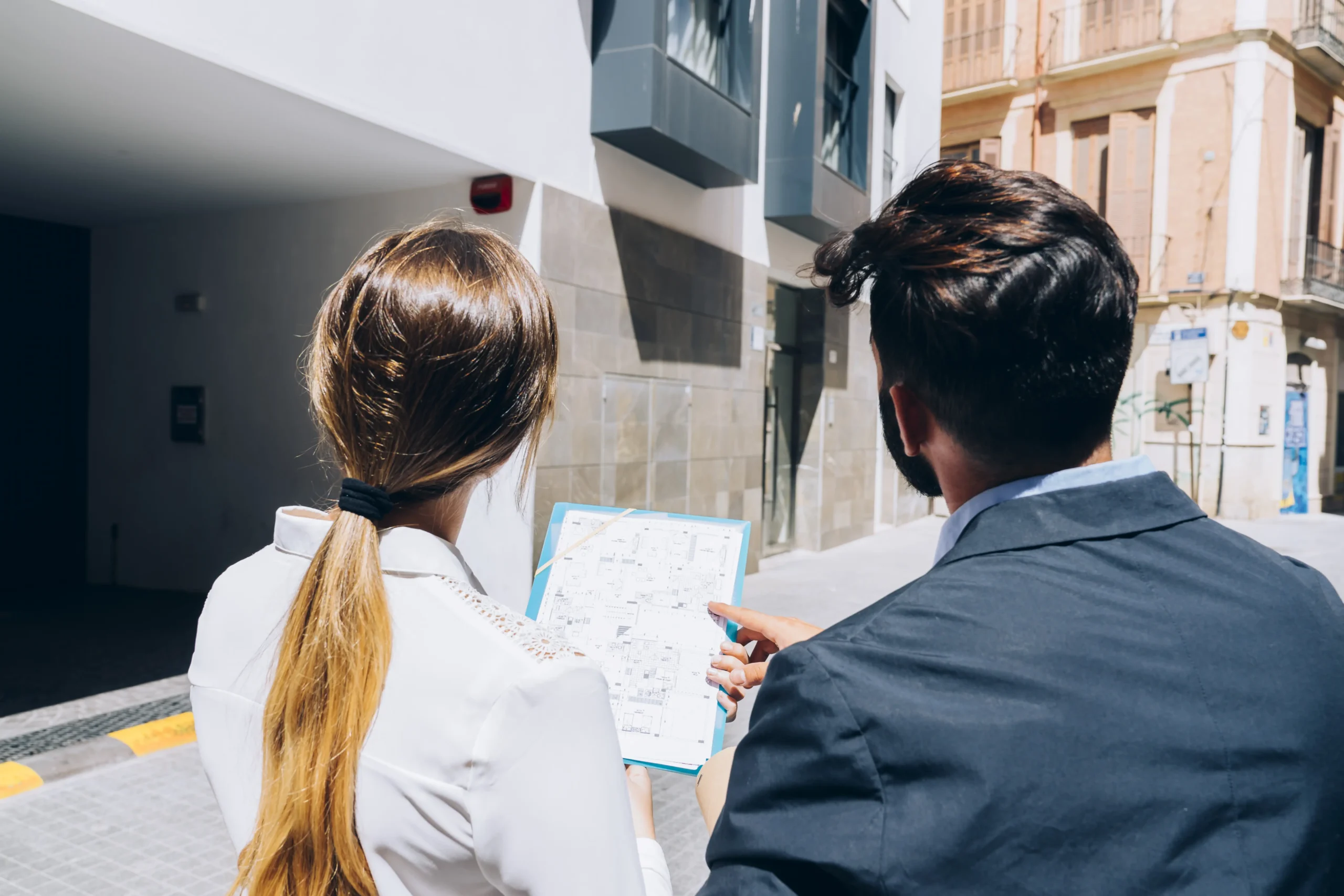 Consultants reviewing blueprints outdoors in front of a building